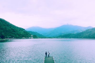 People on lake by mountains against sky