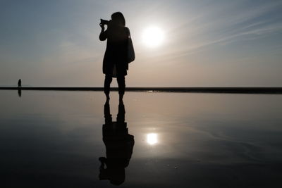 Silhouette man photographing against sky during sunset