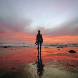 Man standing on beach against dramatic sky during sunset