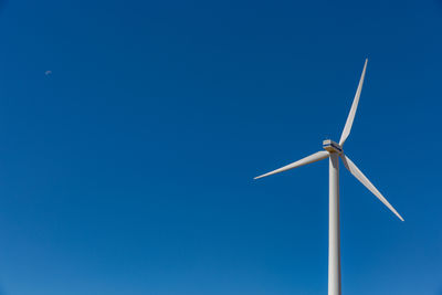 Low angle view of wind turbine against blue sky