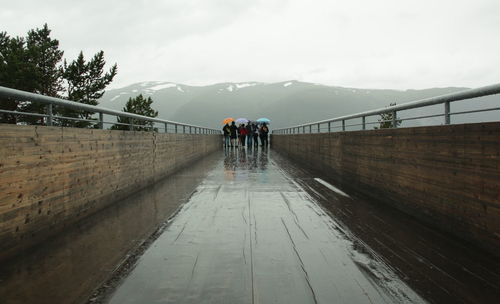 Rear view of people walking on wet footbridge