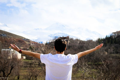Rear view of man with arms outstretched against mountain