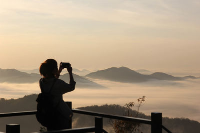 Woman photographing on mountain against sky during sunset