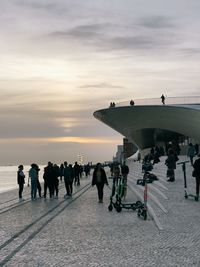 People on promenade by sea against sky during sunset