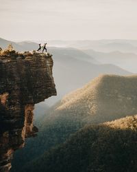 Man standing on cliff by mountains against sky