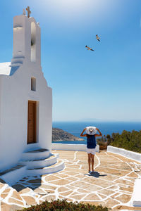 Rear view of woman walking by church against blue sky