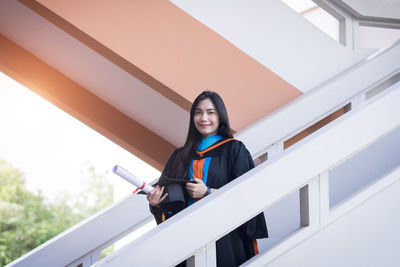 Portrait of young woman standing against railing