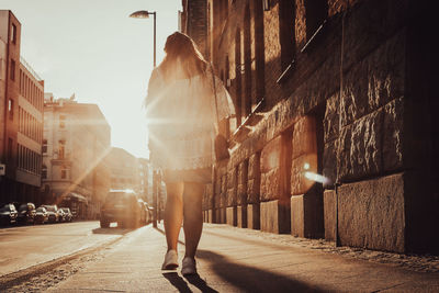 Rear view of woman walking on street amidst buildings at sunset