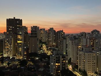 Illuminated buildings in city against sky during sunset