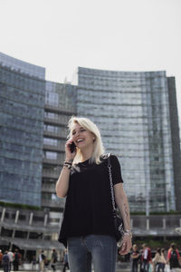 Smiling young woman talking on mobile phone while standing in city