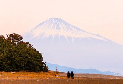 Rear view of people walking on field against snowcapped mountain