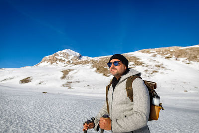 A man walks alone on the snow in the mountains, towards the summit, on a sunny winter day.