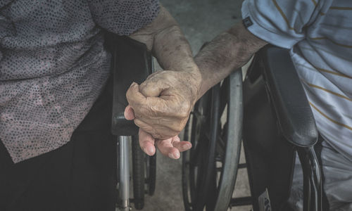 Midsection of senior couple holding hand while sitting on wheel chair