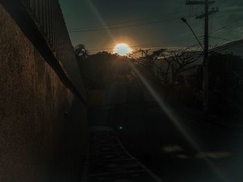 Railroad tracks amidst street against bright sun during sunset