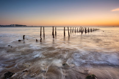 Wooden posts on beach against sky during sunset