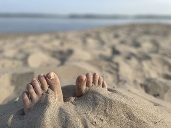 Low section of person relaxing on sand at beach