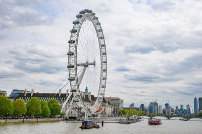 Ferris wheel in city against cloudy sky