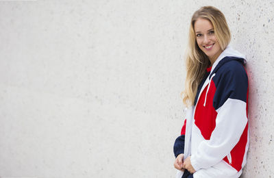 Portrait of a smiling young woman standing against wall