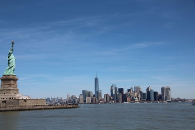 Statue of liberty by river against sky in city