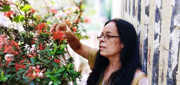 Mature woman looking at flowering plant against wall