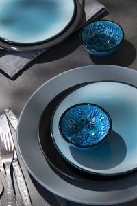 Tableware, different plates in grey blue colors on dark table with geometrical shapes shadows