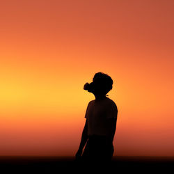 Silhouette man standing against orange sky during sunset