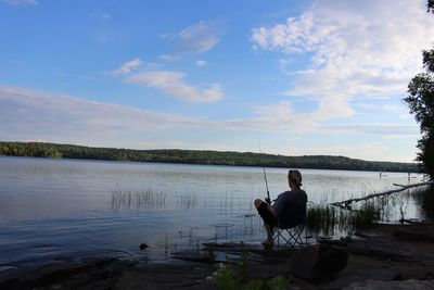 Man sitting by fishing lake against sky
