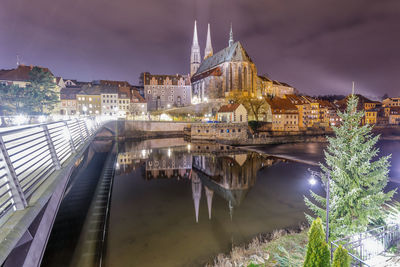 Illuminated buildings by river against sky in city at night