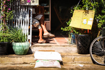 Low section of a man sitting cross-legged in front of his small shop