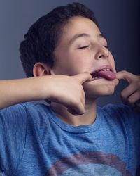 Close-up of boy sticking out tongue while standing against wall