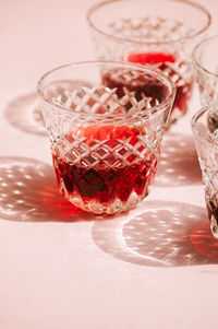 Red wine in a transparent glass with abstract shadows on pink background.