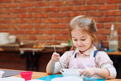 Girl with bowl sitting on table against wall