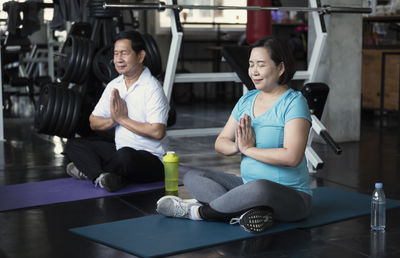 Smiling people meditating while sitting at gym