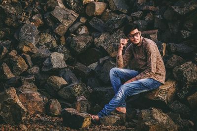 Thoughtful young man looking away while sitting on rock