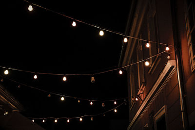 Low angle view of illuminated light bulb hanging at night