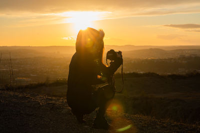 Silhouette woman photographing against sky during sunset