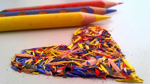 Close-up of multi colored pencils by heart shaped shavings on table