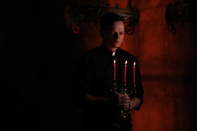 Man holding lit candles while standing in darkroom