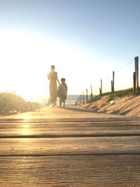 Rear view of people walking on boardwalk against sky