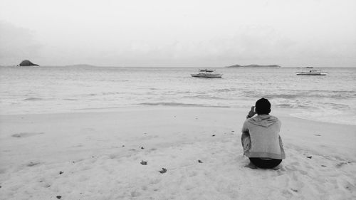 Rear view of man crouching at beach against sky