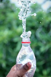 Close-up of hand holding bottle against water