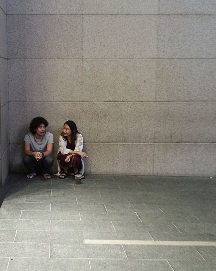 YOUNG WOMAN SITTING ON FLOOR AGAINST WALL