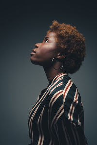 Side view of self assured black female model in striped dress while standing in dark studio