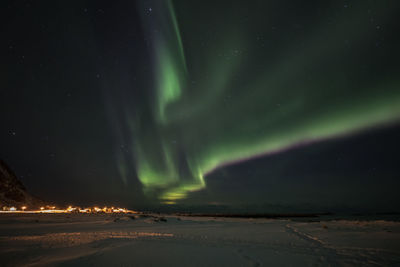 Scenic view of aurora borealis over snow covered landscape against star field at night