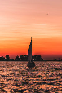 Silhouette sailboat sailing on sea against orange sky