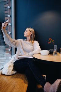 Young woman taking selfie with mobile phone while sitting on table at cafe