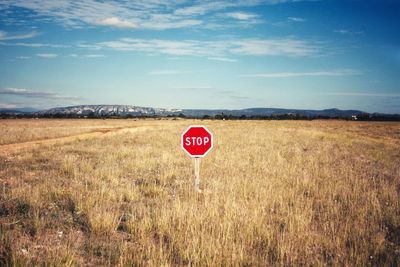 Stop sign on grassy field against sky