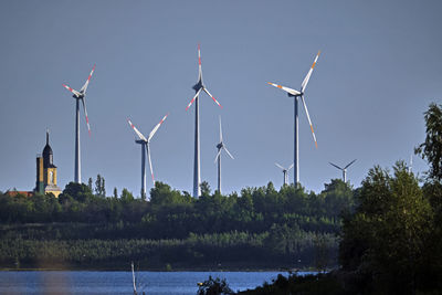 Wind turbines by lake against sky