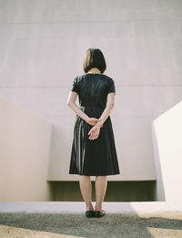 Rear view of woman with hands behind back standing against wall