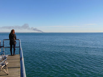 Rear view of woman standing on pier over sea